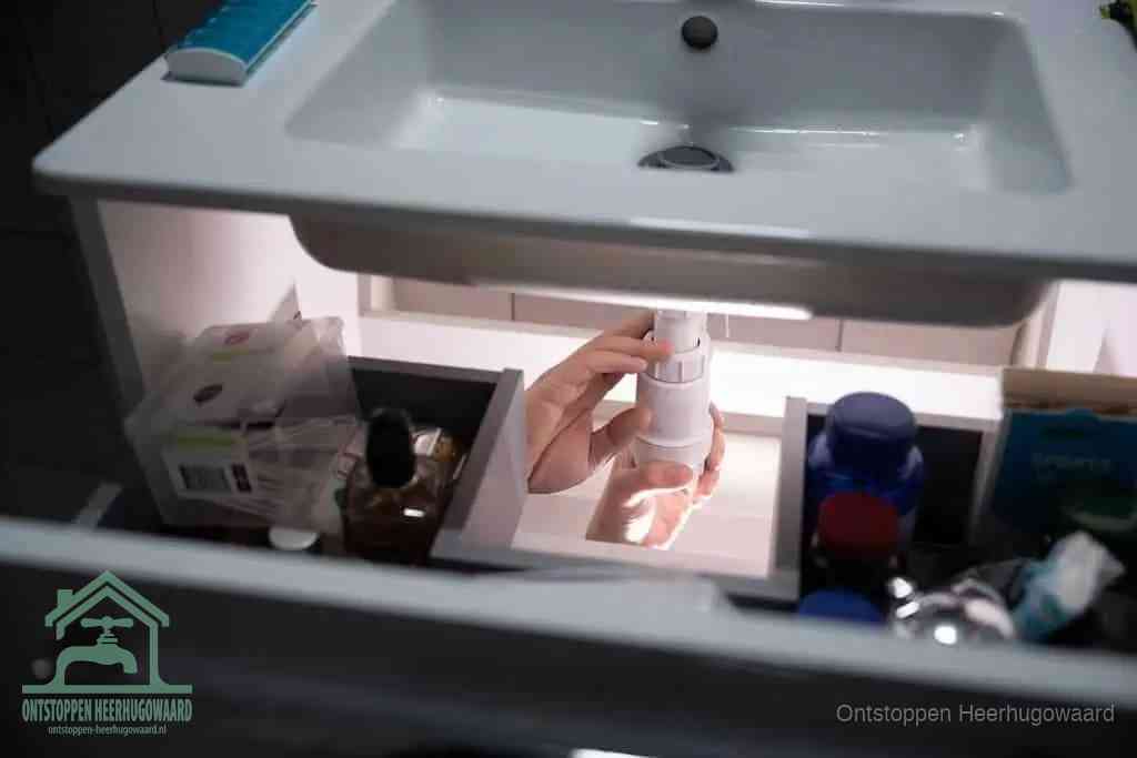 Een pompfles met zeep boven een wastafel, de heet water en afwasmiddel-methode om een vetprop in de afvoer los te maken in Heerhugowaard