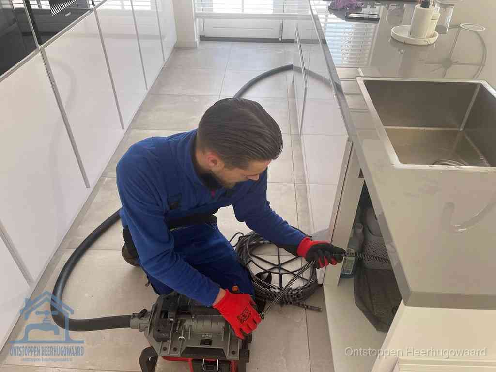 Een monteur ontstopt de keukenafvoer onder de spoelbak met een elektrische veermachine in Heerhugowaard