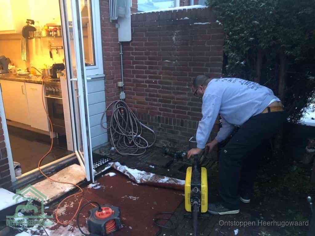 Een monteur werkt buiten bij een open riool-/grondput met een elektrische ontstoppingsmachine om een verborgen afvoerprobleem op te sporen in Heerhugowaard