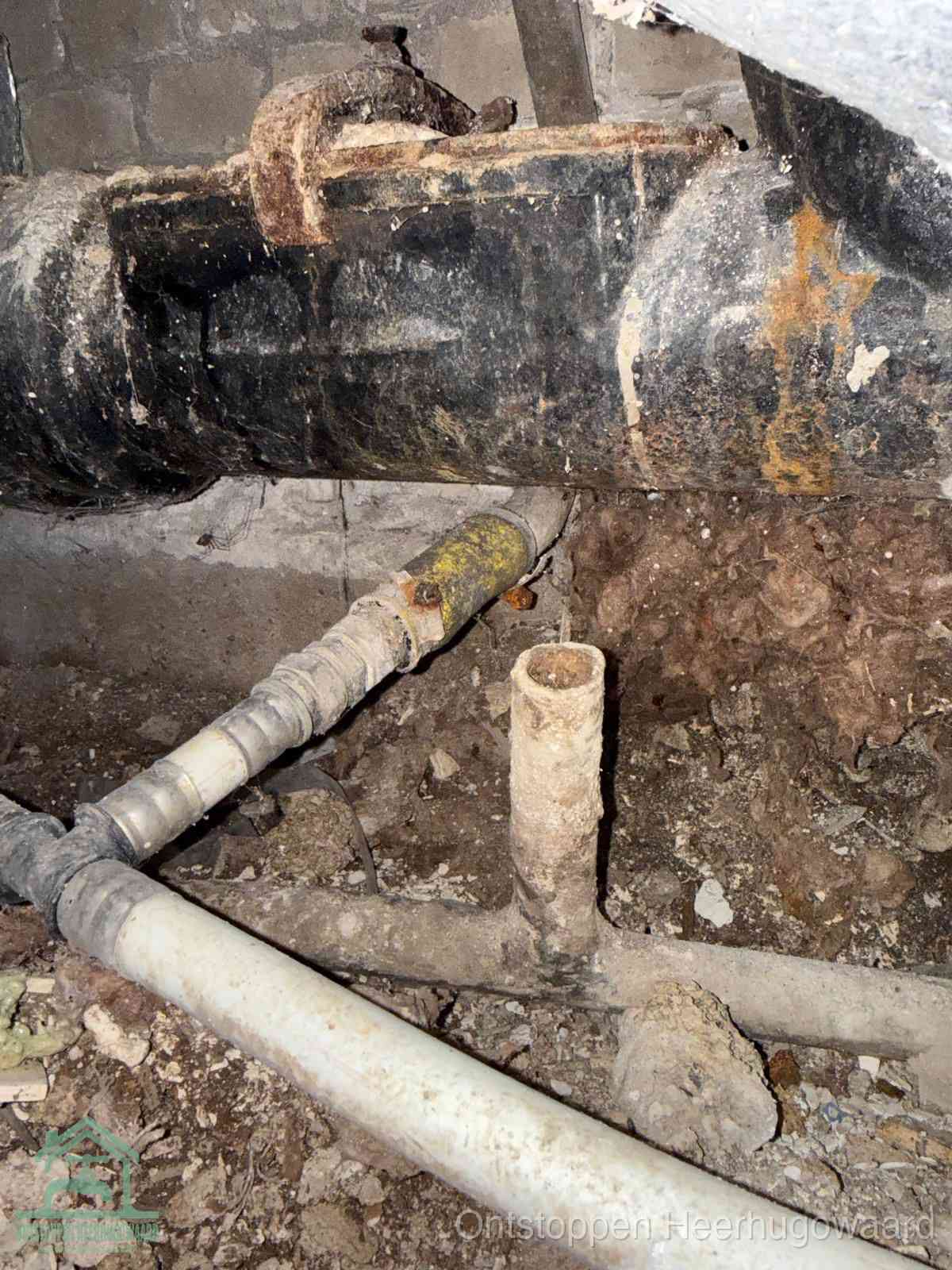 Een dikke zwarte hoofdrioolbuis met roest- en kalkaanslag in een kruipruimte, oorzaak van terugkerende structurele afvoerproblemen in Heerhugowaard