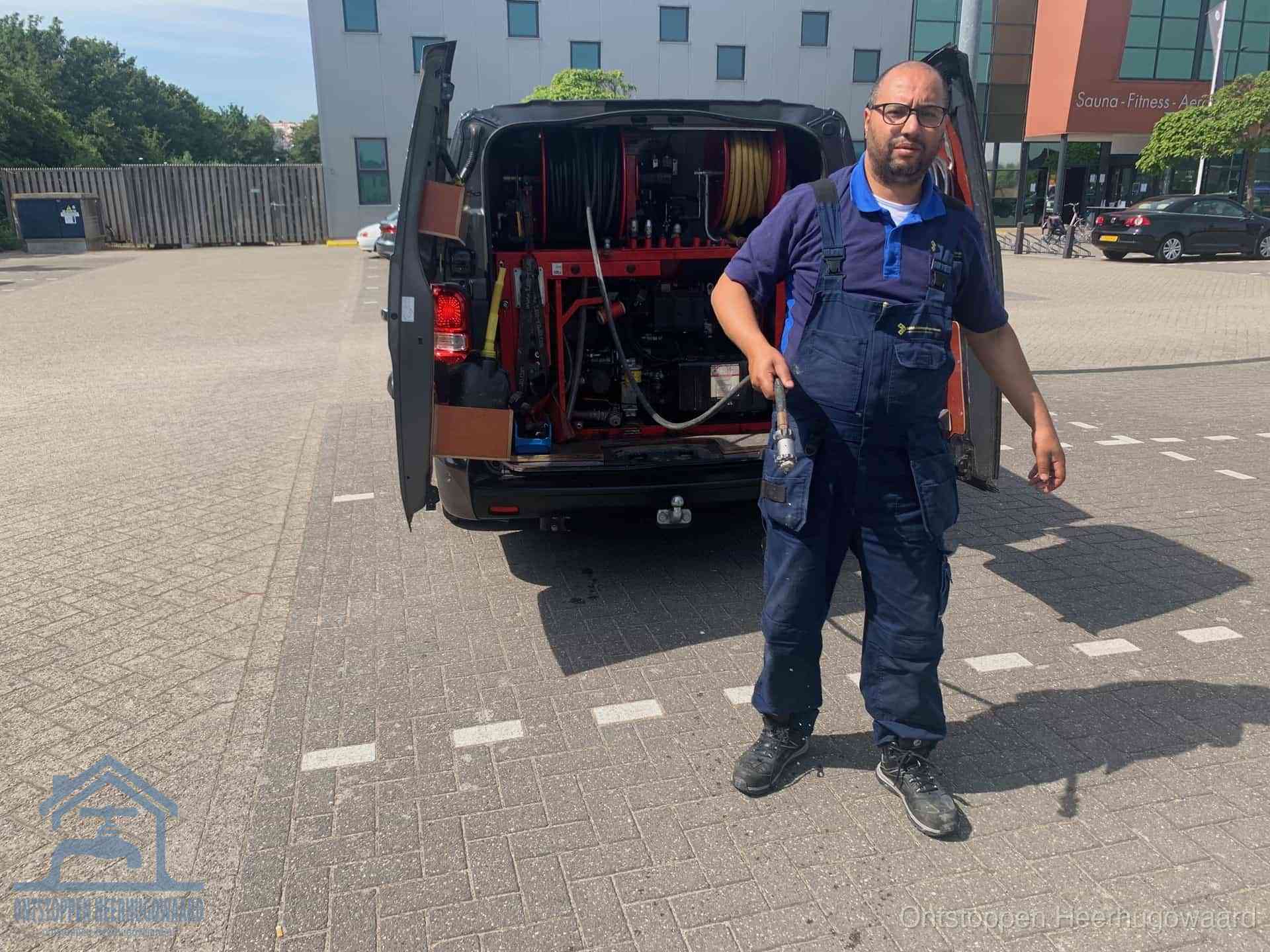Een monteur bij zijn bestelbus met een hogedruk- en rioolreinigingsunit, klaar om de oorzaak van terugkerende wc-verstoppingen aan te pakken in Heerhugowaard