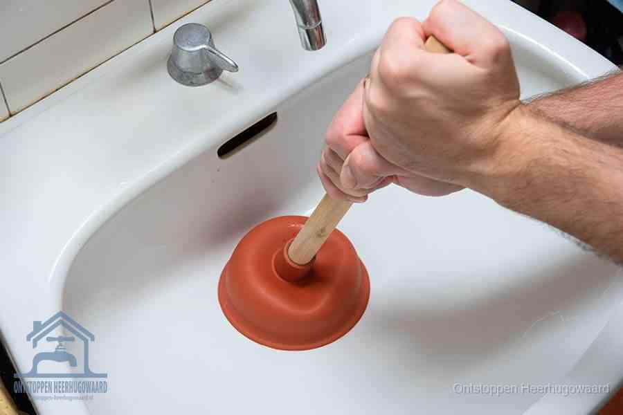 Twee handen gebruiken een rode rubberen plopper op een sanitair-afvoer om het toilet te ontstoppen in Heerhugowaard