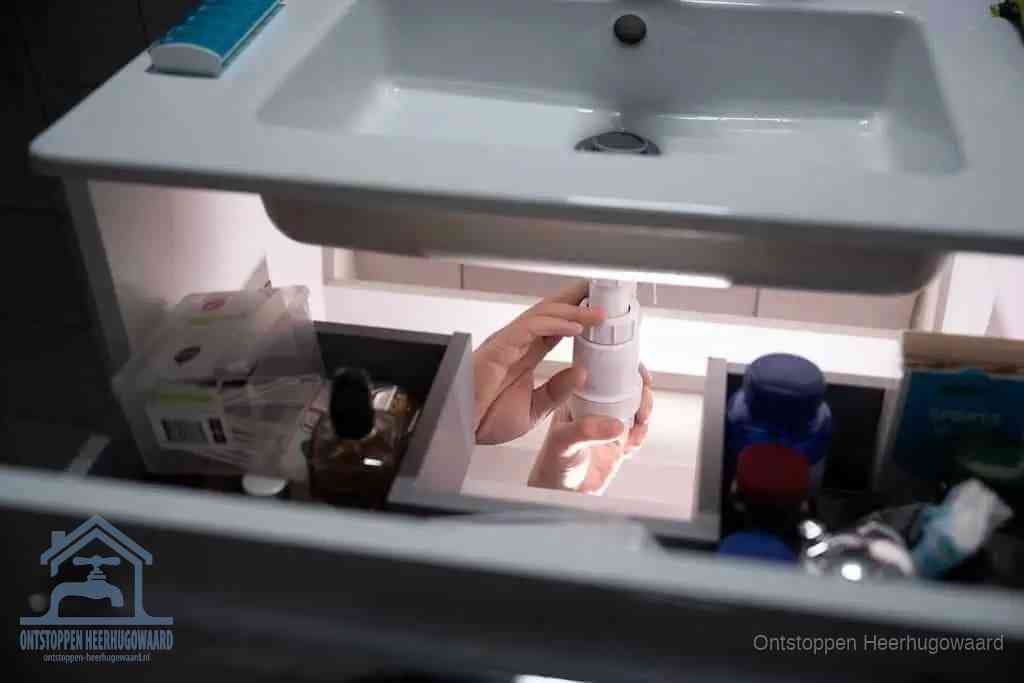 Een pompfles met zeep boven een wastafel in de toiletruimte, de warm water en afwasmiddel-methode om de wc te ontstoppen in Heerhugowaard