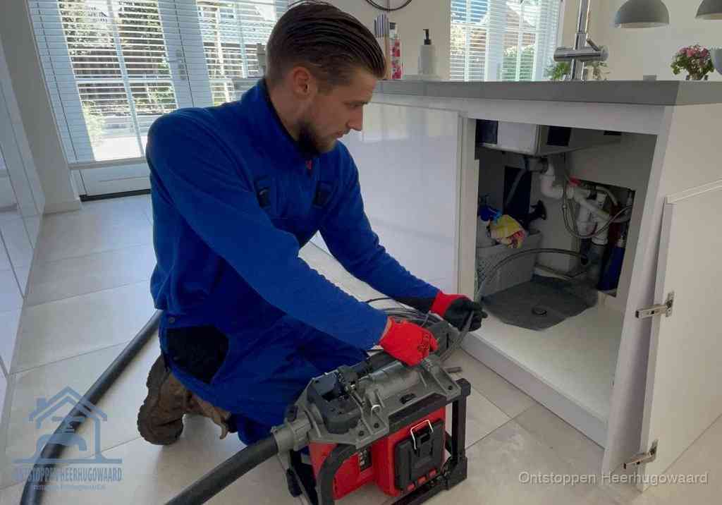 Een monteur voert een professionele elektrische ontstoppingsmachine in de afvoer onder de spoelbak tijdens het gootsteen ontstoppen in Heerhugowaard